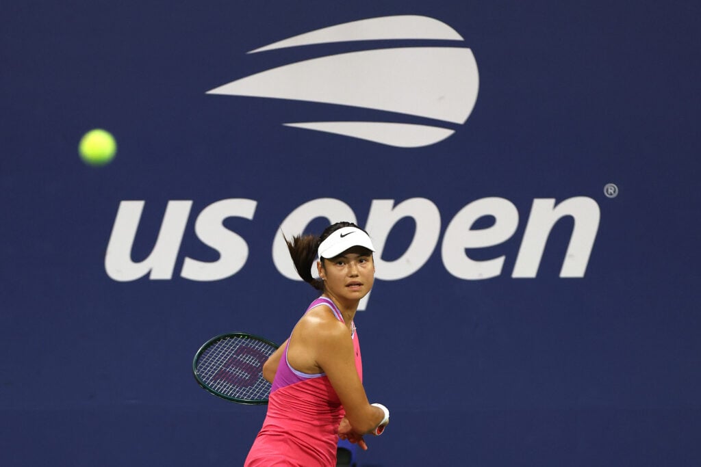 Emma Raducanu prepares to hit a backhand in front of the US Open logo