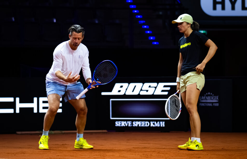 Wim Fisette crouches whilst talking to Iga Swiatek