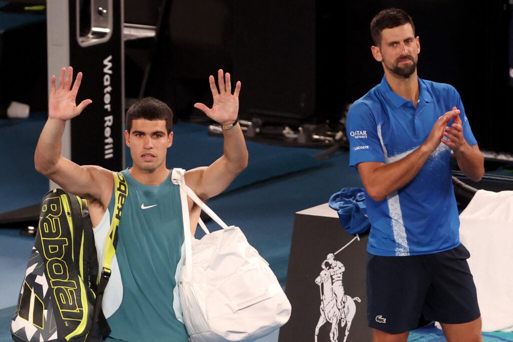 Carlos Alcaraz waves as he leaves the court, with Novak Djokovic clapping
