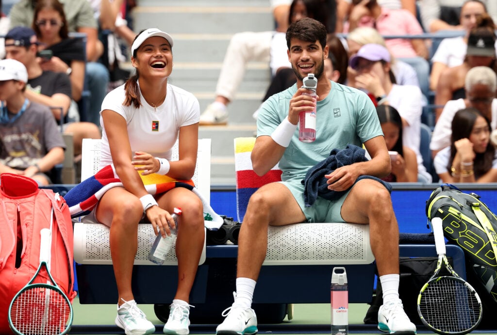 The doubles team of Emma Raducanu of Great Britain and Carlos Alcarez of Spain share a laugh as they sit on the bench in between games during the mixed doubles first round match against Jessica Pegula of the United States and Jack Draper of Great Britain at USTA Billie Jean King National Tennis Center on August 19, 2025 in New York City.