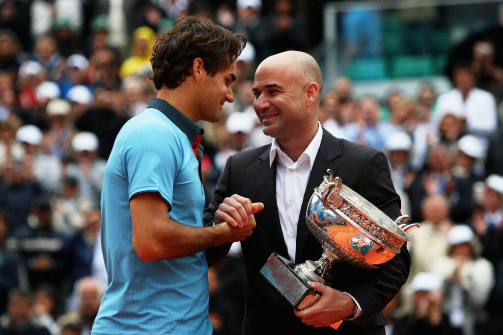 Roger Federer of Switzerland receives the trophy from former champion Andre Agassi following his victory during the Men's Singles Final match against Robin Soderling of Sweden on day fifteen of the French Open at Roland Garros on June 7, 2009 in Paris, France.