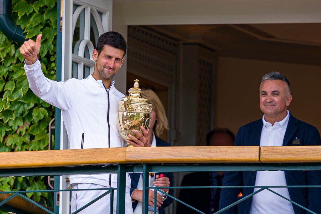 Novak Djokovic of Serbia poses with the trophy and father Srdjan Djokovic as he celebrates victory on the balcony after the Gentlemen's Singles final against Roger Federer of Switzerland during Day thirteen of The Championships - Wimbledon 2019 at All England Lawn Tennis and Croquet Club on July 14, 2019 in London, England.
