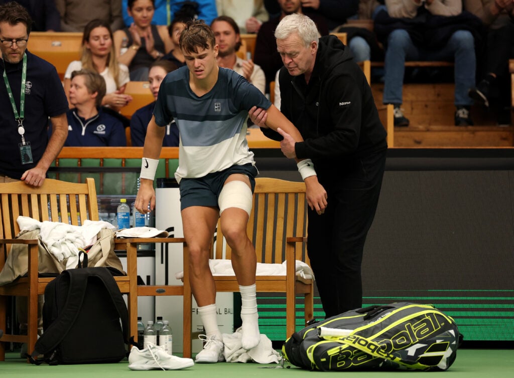 Holger Rune of Denmark is assisted off the court as he is forced to retire following an injury against Ugo Humbert of France during the Men's Singles semi-final match on day eight of the BNP Paribas Nordic Open 2025 at Royal Tennis Hall on October 18, 2025 in Stockholm, Sweden.