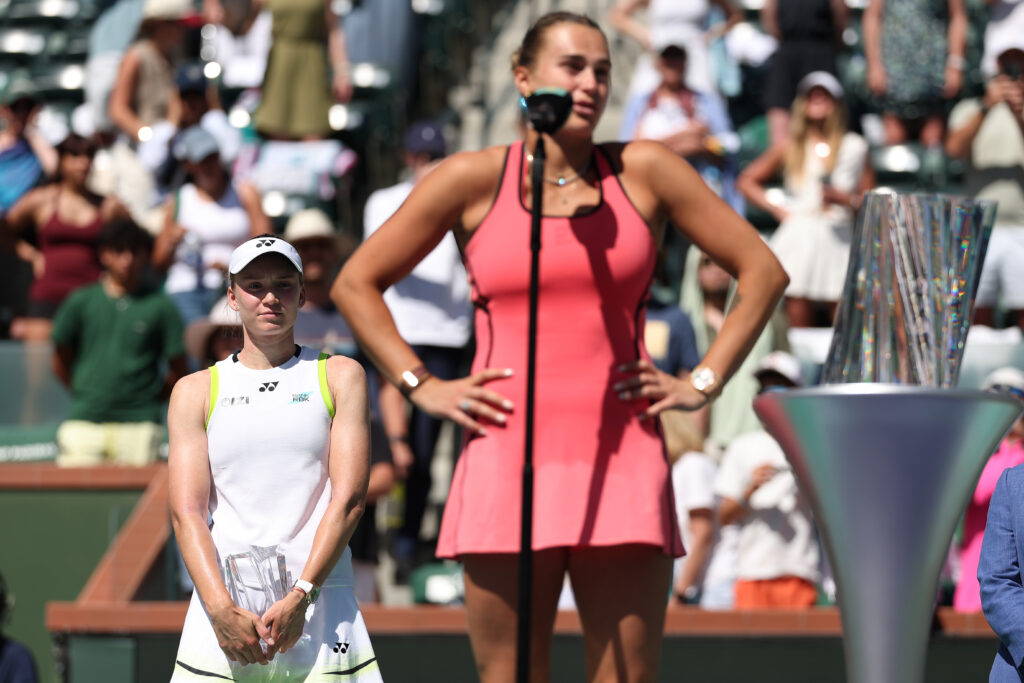 Second place winner Elena Rybakina of Kazakhstan looks on from the back as Aryna Sabalenka talks to the crowd after winning the championship following their Women's Singles Finals match on Day 12 of the BNP Paribas Open at Indian Wells Tennis Garden on March 15, 2026 in Indian Wells, California.