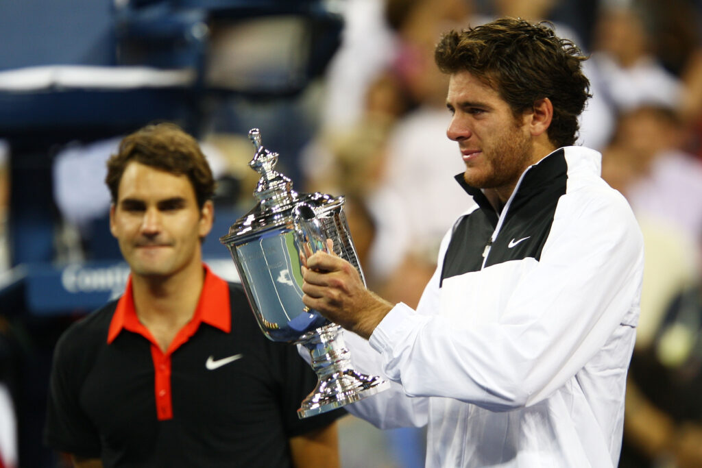 Juan Martin Del Potro of Argentina holds the championship trophy as Roger Federer of Switzerland looks on in the Men's Singles final on day fifteen of the 2009 U.S. Open at the USTA Billie Jean King National Tennis Center on September 14, 2009 in the Flushing neighborhood of the Queens borough of New York City. Del Potro defeated Federer 3-6, 7-6 (7), 4-6, 7-6 (7), 6-2.