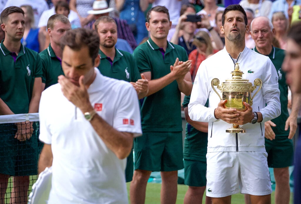 Novak Djokovic of Serbia holds the trophy as he watches watches Roger Federer of Switzerland after the Men's Singles Final on Centre Court during the Wimbledon Lawn Tennis Championships