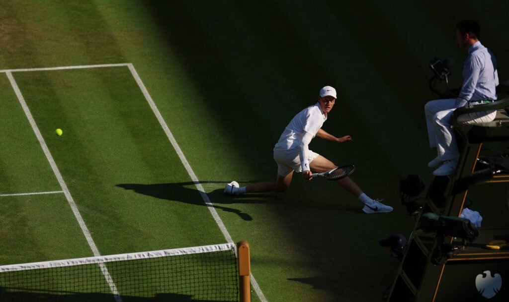 Jannik Sinner of Italy slides as he plays a backhand against Novak Djokovic of Serbia during the Gentlemen's Singles semi-final match on day twelve of The Championships Wimbledon 2025 at All England Lawn Tennis and Croquet Club on July 11, 2025 in London, England.